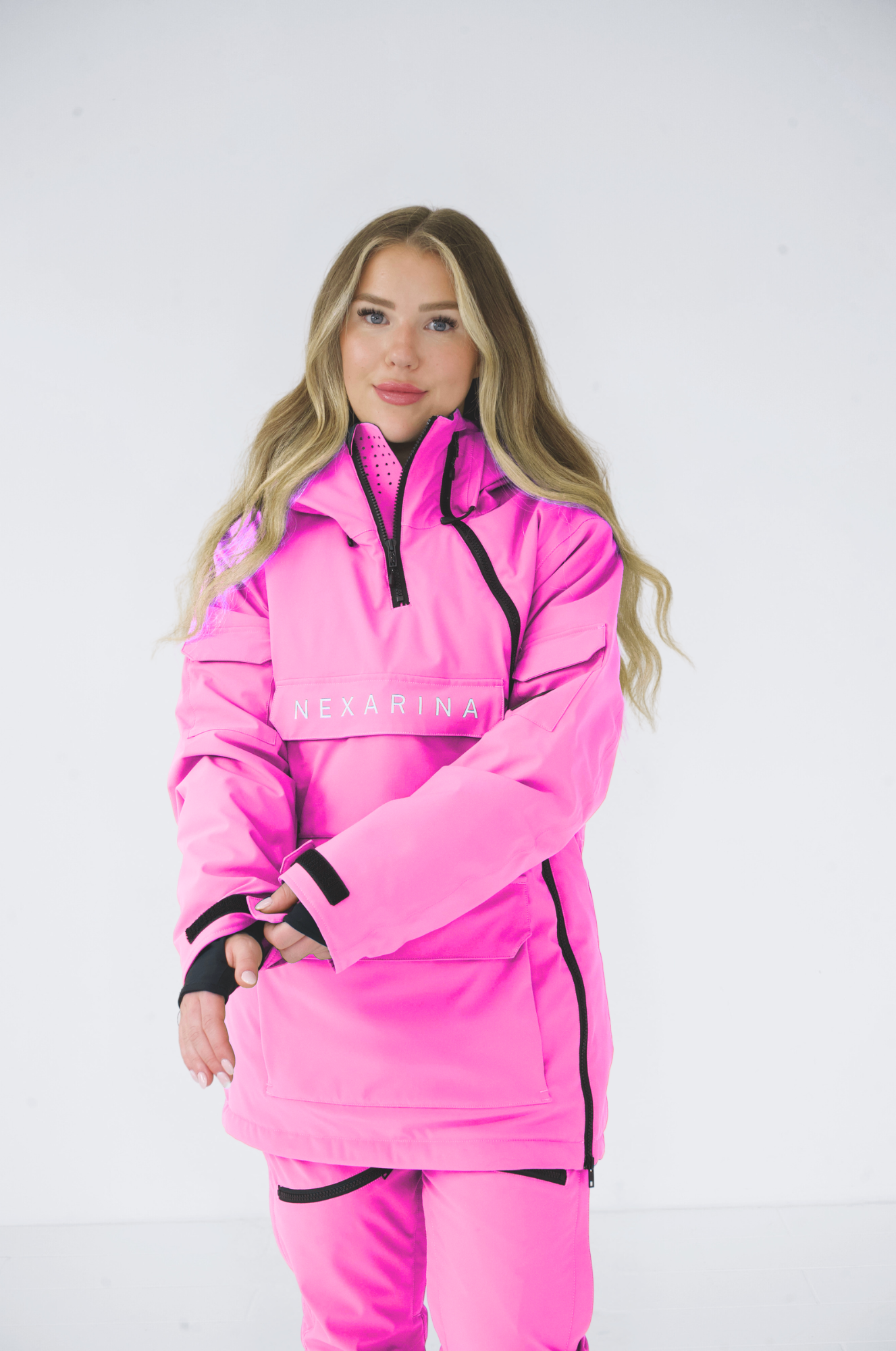 Woman in a pink Nexarina ski jacket standing with arms crossed, smiling towards the camera, against a white background.
