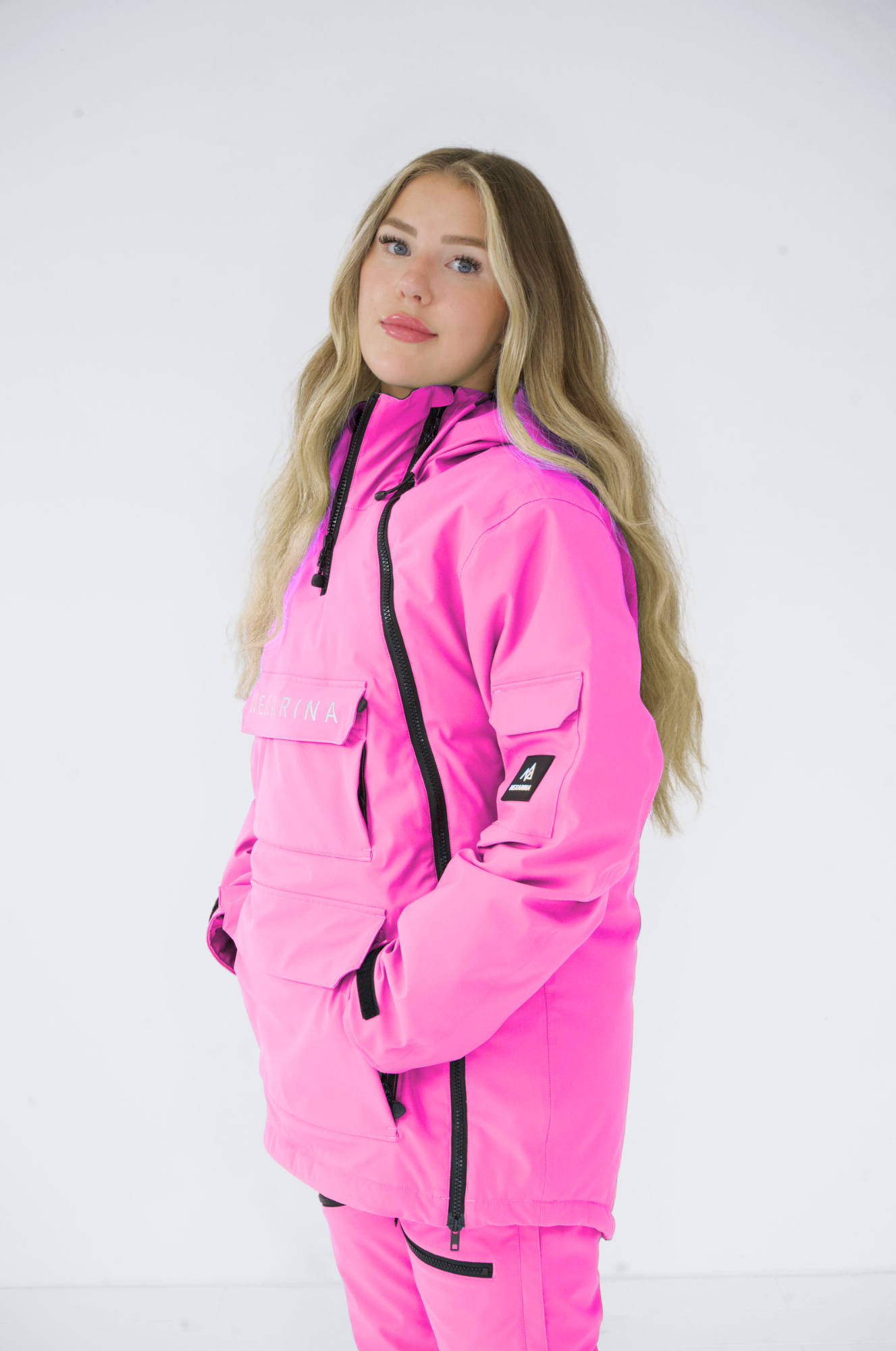 Side profile of a woman in a pink Nexarina snowboard jacket, posed against a white backdrop
