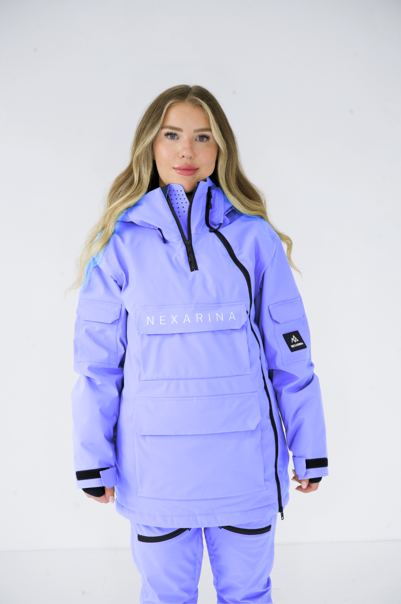 Female model in Nexarina's purple snowboard gear, showcasing the jacket's ventilated collar and multiple pockets, ideal for winter sports.