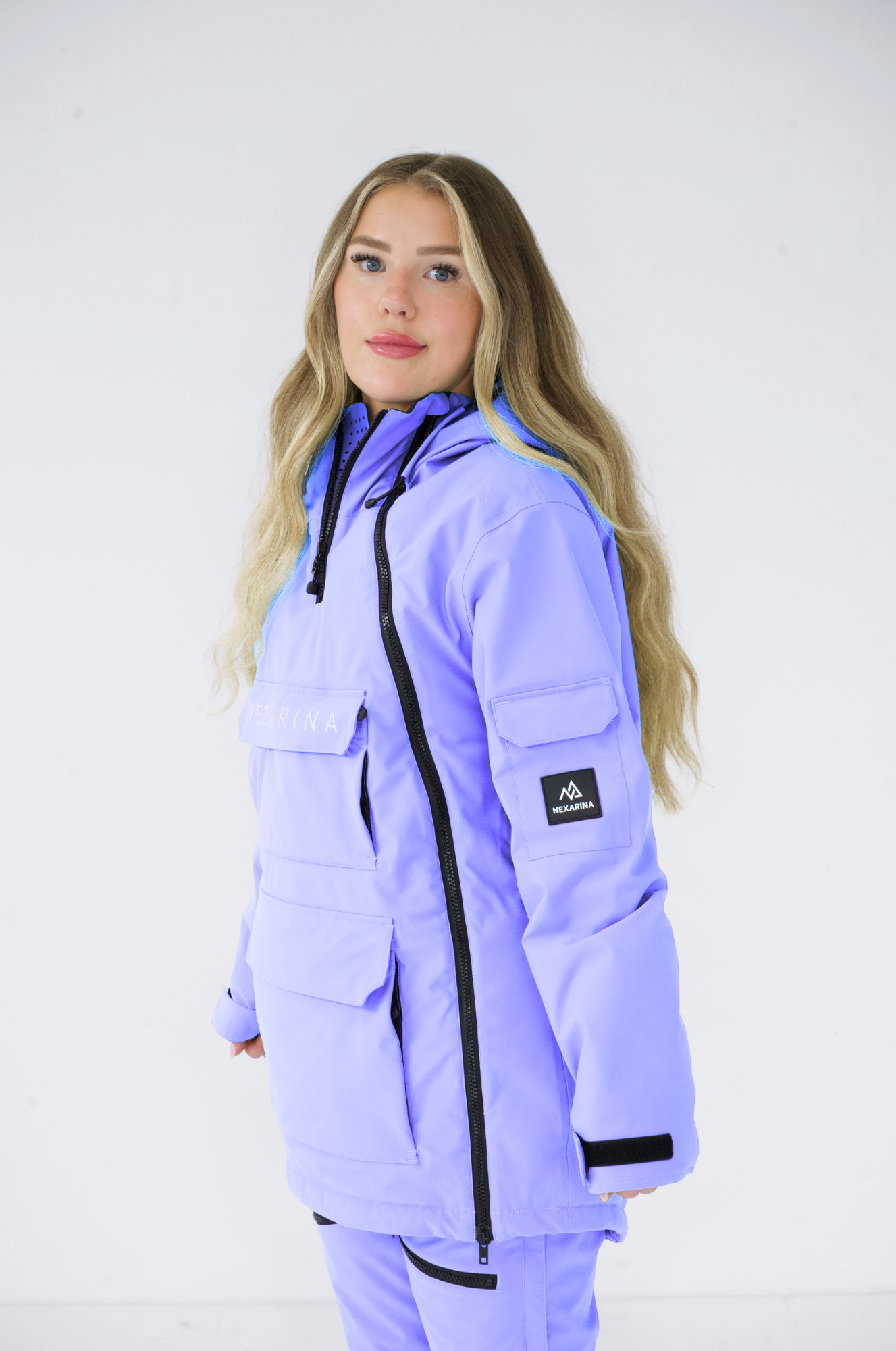  side view of a female model wearing Nexarina purple snowboarding gear, showcasing the sleek design and side features of the jacket and pants.