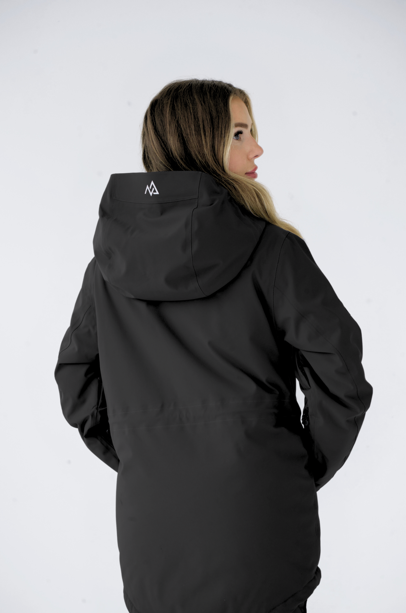Rear view of a woman wearing a black Nexarina jacket, showing the adjustable hood and the brand logo on the upper back
