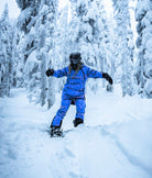 Person in artctic blue snowsuit snowboarding through a snowy forest