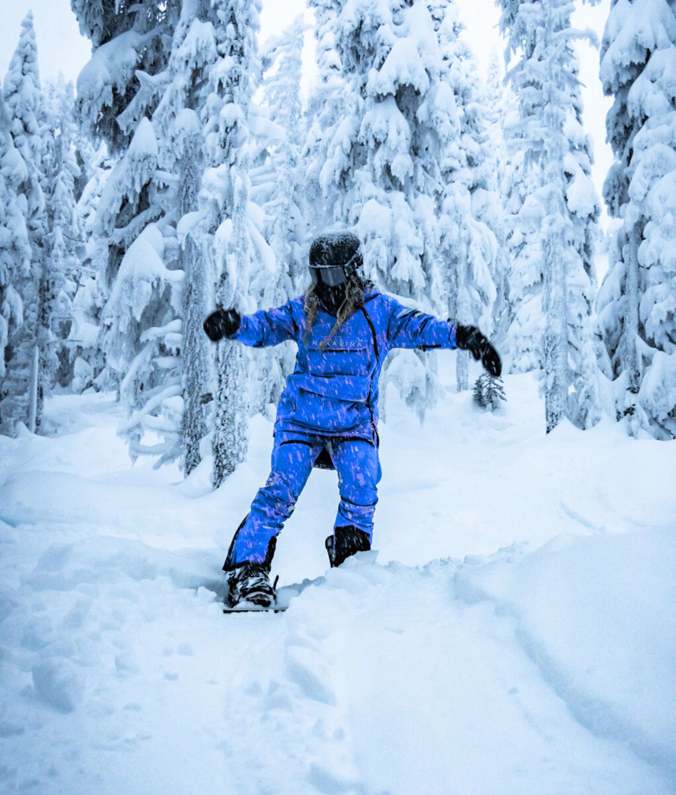 Person in artctic blue snowsuit snowboarding through a snowy forest