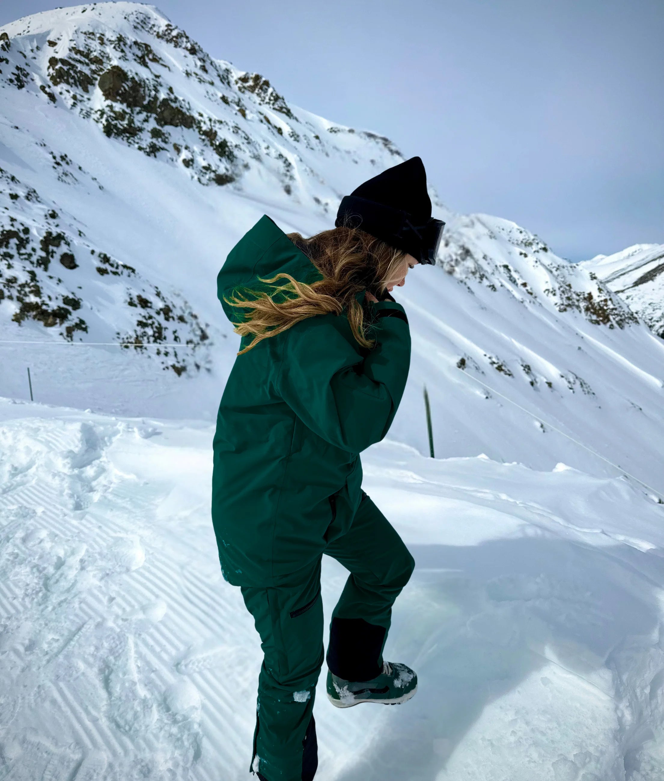 Woman wearing Nexarina Avani snowpants in emerald green with mountain backdrop.