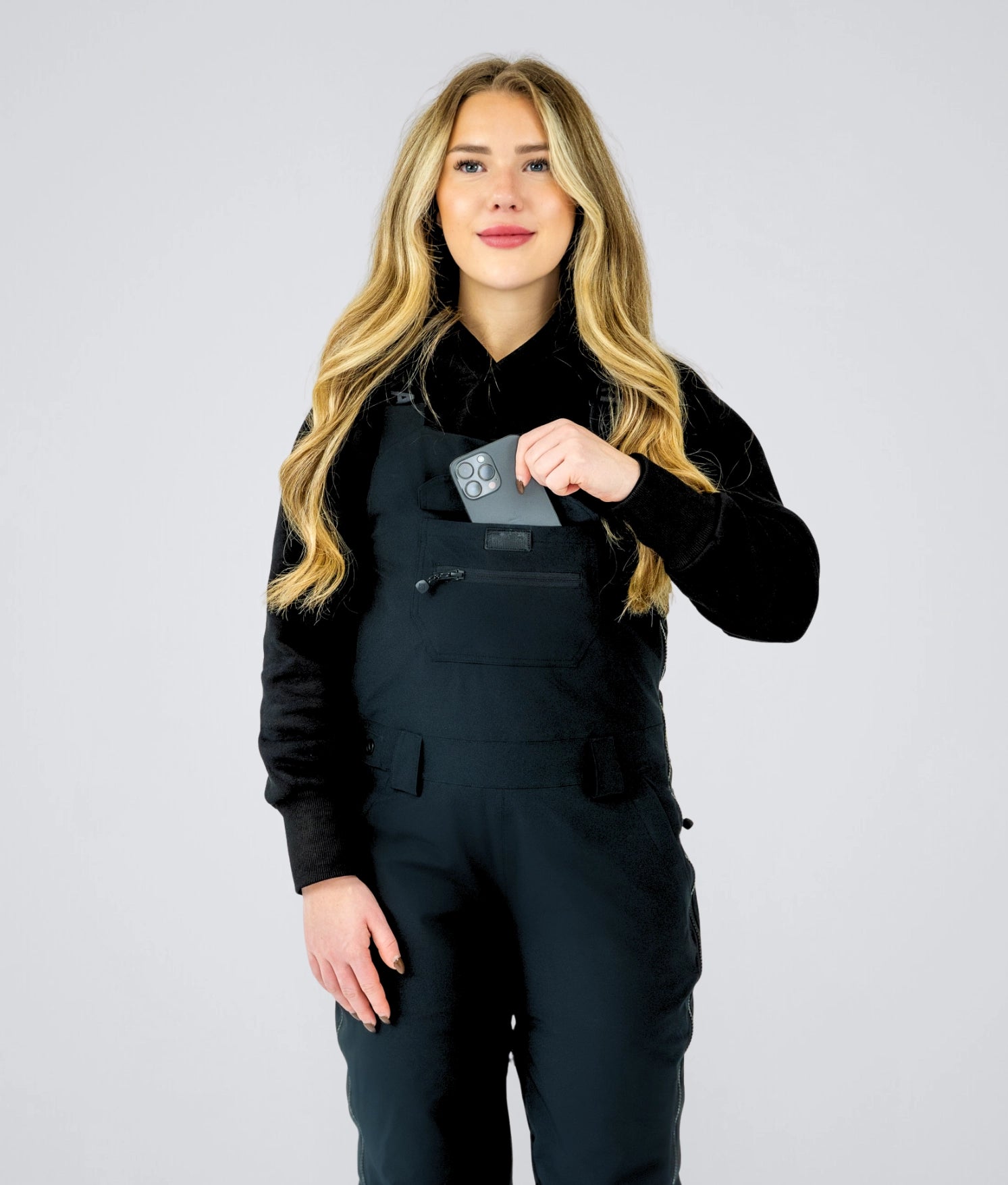 Front view of Nexarina Everette women’s bib snow pants in black, showing chest pocket storage and women’s performance fit.