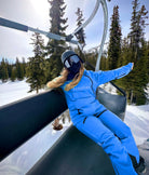 A snowboarder lounges on a ski lift in blue Avani snow pants, built for durability, comfort, and weather resistance.